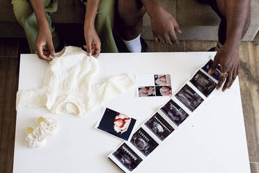 Couple with baby clothing and ultrasound pictures on table - GGGF01220