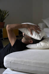 Depressiver Mann, der sein Gesicht mit einem Kissen bedeckt und sich an ein Sofa lehnt - VEGF05852