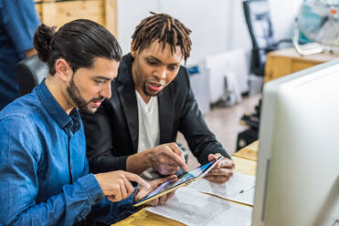 Glad diverse male employees in formal wear surfing tablet while working together on business project at table in light modern office - ADSF36489