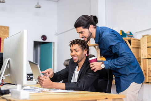 Glad diverse männliche Mitarbeiter in formaler Kleidung Surfen Tablet während der Arbeit zusammen auf Business-Projekt am Tisch in hellen modernen Büro - ADSF36492