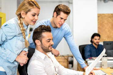 Group of content woman and men in formal wear working together with documents at table in modern light spacious office - ADSF36499