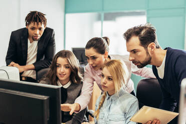 Konzentrierte multirassische Männer und Frauen in formeller Kleidung beim Surfen am Computer, während sie gemeinsam an einem Geschäftsprojekt in einem hellen modernen Büro arbeiten - ADSF36527