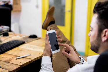 Seitenansicht der Ernte männlichen Arbeiter Surfen im Internet auf Handy mit schwarzem Bildschirm, während an Holztisch in modernen Arbeitsbereich sitzen - ADSF36542