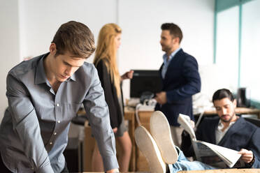 Fokussierter männlicher Arbeiter in formeller Kleidung, der sich Notizen in Dokumenten auf dem Tisch macht, während er in einem hellen, modernen Büro mit Kollegen arbeitet - ADSF36552