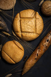 Top view background of assorted bread loaves and baguette placed near heap of wheat spikes on black surface in studio - ADSF36607