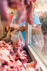 Unbekannter reifer Kunde, der beim Besuch einer Metzgerei auf dem Markt eine Tasche mit Frischfleisch füllt - ADSF36667