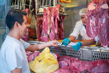 Verkäufer in Handschuhen erhält Barzahlung an männlichen Kunden beim Verkauf von Fleisch auf dem Markt - ADSF36673