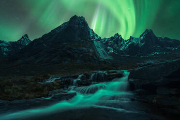 Scenic scenery of clear river flowing through stony cliffs on Lofoten island under dynamic flickers of aurora borealis lights - ADSF36812