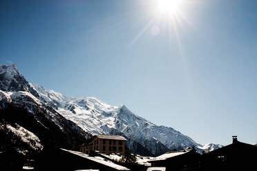 Wohngebäude in der Nähe von rauen felsigen Bergen mit weißem Schnee bedeckt gegen sonnigen blauen Himmel in der Landschaft auf Wintertag - ADSF36836