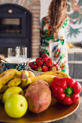 Set von bunten reifen Früchten und Gemüse auf dem Tisch in der Nähe von Obst und Geschirr in hellen Küche mit gesichtslosen Frau platziert - ADSF36848