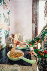 Crop anonyme weibliche Koch rühren köstliche Quinoa mit Spatel in der Pfanne auf Induktionsherd beim Kochen in hellen Küche - ADSF36862