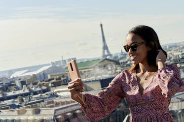 Young woman taking selfie through smart phone with Eiffel Tower in background, Paris, France - KIJF04494