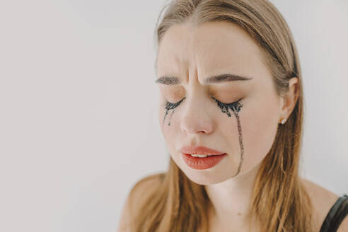 Traurige junge Frau mit verschmierter Wimperntusche, die vor einer Wand weint - ORF00032