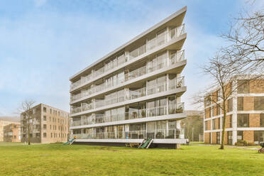 Kreative Gestaltung moderner mehrstöckiger Hausfassaden in der Nähe von grünem Gras unter blauem Himmel in den Niederlanden - ADSF36884