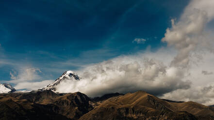 Weiße Wolken schweben im blauen Himmel in der Nähe von schneebedeckten Gipfeln der atemberaubenden Bergkette in der Tageszeit im Hochland - ADSF36900