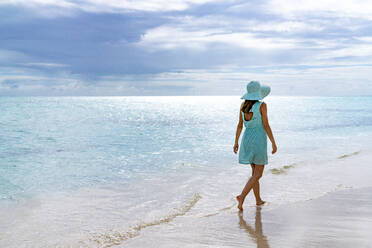 Woman walking on a white sand beach under the cloudy sky at sunset, Barbuda, Antigua and Barbuda, West Indies, Caribbean, Central America - RHPLF22839