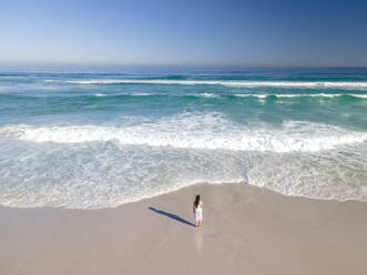 Luftaufnahme einer Frau, die am Strand vor den Wellen steht, Kapstadt, Südafrika. - AAEF15519