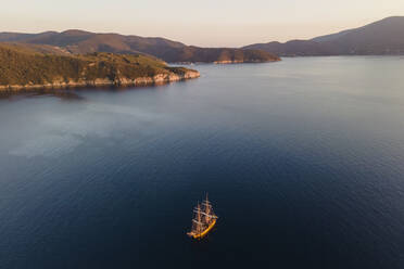 Luftaufnahme eines Piratenschiffs, das bei Sonnenuntergang an der Küste von Capo D'Enfola, Insel Elba, Toskana, Italien, entlangfährt. - AAEF15708