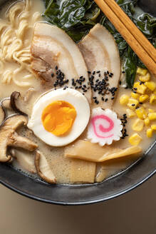 Von oben der appetitlichen japanischen Ramen mit gekochtem Ei und Pilzen in Schüssel mit hölzernen Stäbchen gegen beige Hintergrund serviert - ADSF36961