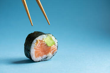 Leckere japanische Futomaki norwegischen Sushi-Rolle mit frischem Lachs und Avocado gegen blauen Hintergrund im Studio mit hölzernen Stäbchen platziert - ADSF36973