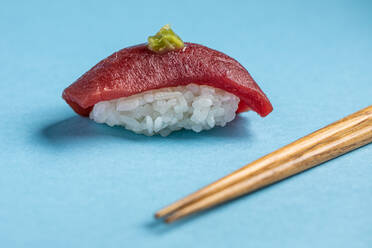 Traditionelle japanische köstliche Bluefin Nigiri mit Reis und frischem Thunfisch mit würzigem Wasabi serviert in der Nähe von Stäbchen auf blauem Hintergrund in hellem Studio - ADSF36976