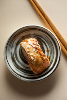 Draufsicht auf leckere japanische Nigiri-Sushi mit geräuchertem Lachs und flambierter Gänsestopfleber, serviert auf einem Teller mit Stäbchen in einem Restaurant - ADSF36980