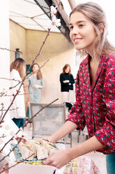 Seitenansicht einer positiv gestimmten, fröhlichen Frau, die während eines Banketts auf der Terrasse eines Gebäudes an einem Sommertag leckere Tortilla-Rollen auf dem Tisch serviert - ADSF36998