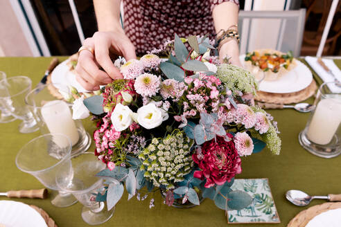 Cropped unerkennbar Frau in Kleidern arrangieren Tisch mit frischen Blumen und leckere Gerichte auf der Terrasse des Gebäudes auf Sommertag - ADSF37002