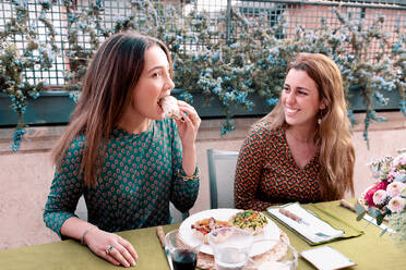 Positive Freundinnen mit Rotwein im Gespräch beim Abendessen am Tisch mit leckerem Essen auf der Terrasse - ADSF37009