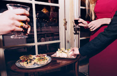 Crop anonyme Freunde mit Weingläsern stehen in der Nähe von Tisch mit verschiedenen leckeren Snacks beim Feiern festliche Veranstaltung zusammen in modernen Restaurant - ADSF37025