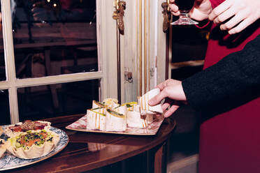 Crop anonyme Freunde mit Weingläsern stehen in der Nähe von Tisch mit verschiedenen leckeren Snacks beim Feiern festliche Veranstaltung zusammen in modernen Restaurant - ADSF37026