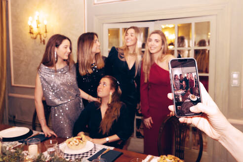 Gruppe positiver weiblicher Freunde, die ein Foto mit dem Smartphone machen, während sie sich während des Abendessens im Restaurant am Tisch versammeln - ADSF37028