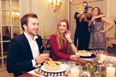 Paar am Tisch mit leckerem Essen und Trinken, während eine Gruppe positiver Freunde beim Abendessen im Restaurant ein Selfie mit dem Smartphone macht - ADSF37030
