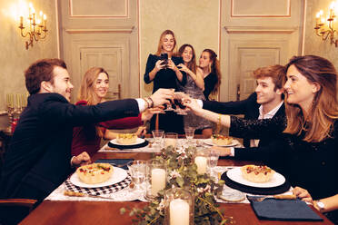 Group of positive friends looking at each other and toasting with wineglasses at table with tasty food during dinner in restaurant - ADSF37031