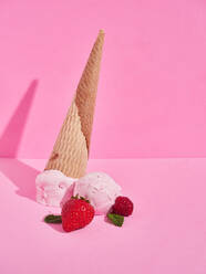 Leckere süße Erdbeereis Kugeln mit gefallenen knusprigen Kegel in der Nähe von reifen Beeren gegen rosa Hintergrund mit Schatten im Studio - ADSF37072