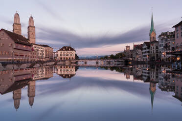 Malerische Stadtlandschaft mit alten Wohngebäuden und romanischer Großmünsterkirche, die sich im Fluss vor dem Sonnenuntergang spiegelt, in Zürich - ADSF37179