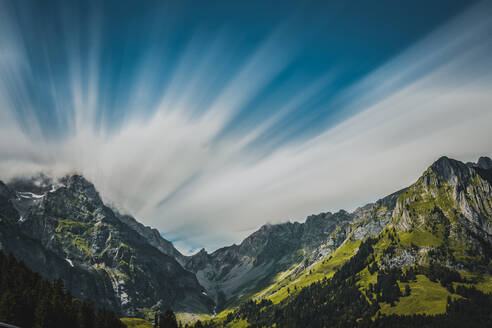 Atemberaubende Kulisse von blauem Himmel über massiven grünen Bergen mit schneebedeckten Gipfeln in der Schweiz - ADSF37183