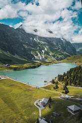Spektakuläre Landschaft des ruhigen Trubsees mit türkisfarbenem Wasser, umgeben von massiven grünen Bergen und Nadelbäumen vor wolkenverhangenem blauem Himmel in der Schweiz - ADSF37185
