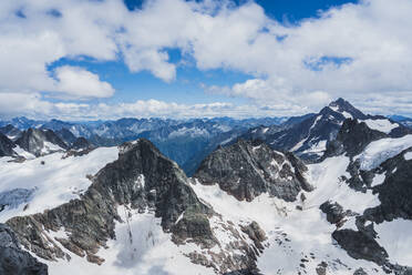 Atemberaubende Landschaft von flauschigen weißen Wolken schweben im blauen Himmel über massiven grünen Bergen mit schneebedeckten Gipfeln in der Schweiz - ADSF37186