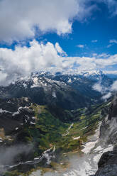 Atemberaubende Landschaft von flauschigen weißen Wolken schweben im blauen Himmel über massiven grünen Bergen mit schneebedeckten Gipfeln in der Schweiz - ADSF37187