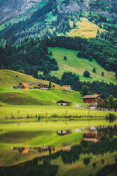 Spektakuläre Landschaft von kleinen Wohnhäusern auf grasbewachsenen Wiese umgeben von massiven grünen felsigen Berge spiegeln sich in ruhigen See in der Schweiz gelegen - ADSF37190