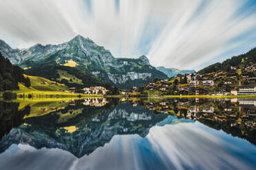 Spektakuläre Landschaft von kleinen Wohnhäusern auf grasbewachsenen Wiese umgeben von massiven grünen felsigen Berge spiegeln sich in ruhigen See in der Schweiz gelegen - ADSF37191