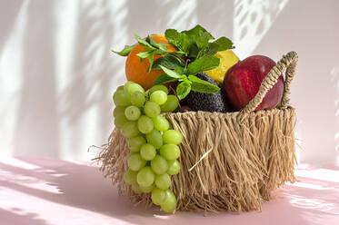 Stillleben von verschiedenen reifen Früchten und Trauben in Weidenkorb mit grüner Minze Blätter auf dem Tisch gegen weißen Hintergrund mit Schatten gelegt - ADSF37206