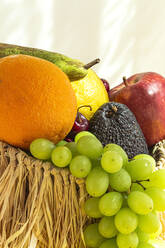 Stillleben von verschiedenen reifen Früchten und Trauben in Weidenkorb mit grünen Minzblättern auf Tisch gegen gelben Hintergrund mit Schatten platziert - ADSF37209