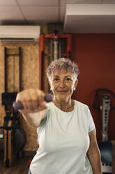 Cheerful motivated elderly woman with short hair in activewear smiling and looking at camera while exercising on pulley machine in modern gym - ADSF37306