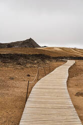 Schmaler leerer Holzweg durch trockenes vulkanisches Gelände in einem Gebirgstal bei bedecktem Himmel in Island - ADSF37327