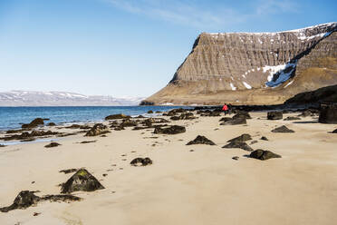 Rough rocky mountains covered with snow located on sandy shore near sea against blue sky in nature of Iceland on winter day - ADSF37333
