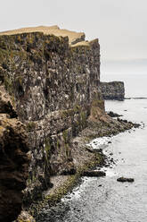 Rough rocky cliff with uneven surface located on shore near sea under overcast sky in coastal area in nature of Iceland - ADSF37335