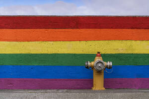 Traditioneller Hydrant auf der Straße in der Nähe der Mauer mit gemaltem LGBT-Regenbogen-Hintergrund am Straßenrand - ADSF37348