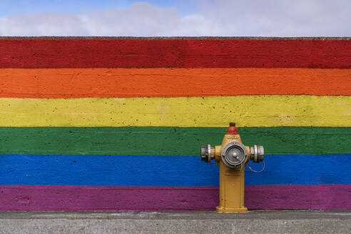 Traditioneller Hydrant auf der Straße in der Nähe der Mauer mit gemaltem LGBT-Regenbogen-Hintergrund am Straßenrand - ADSF37348